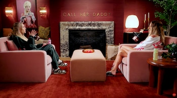 Dos mujeres sentadas en sillones rosas enfrentadas en una sala roja con una chimenea. Una lleva chándal oscuro, la otra una sudadera blanca. Detrás, un letrero que dice 'CALL HER DADDY'