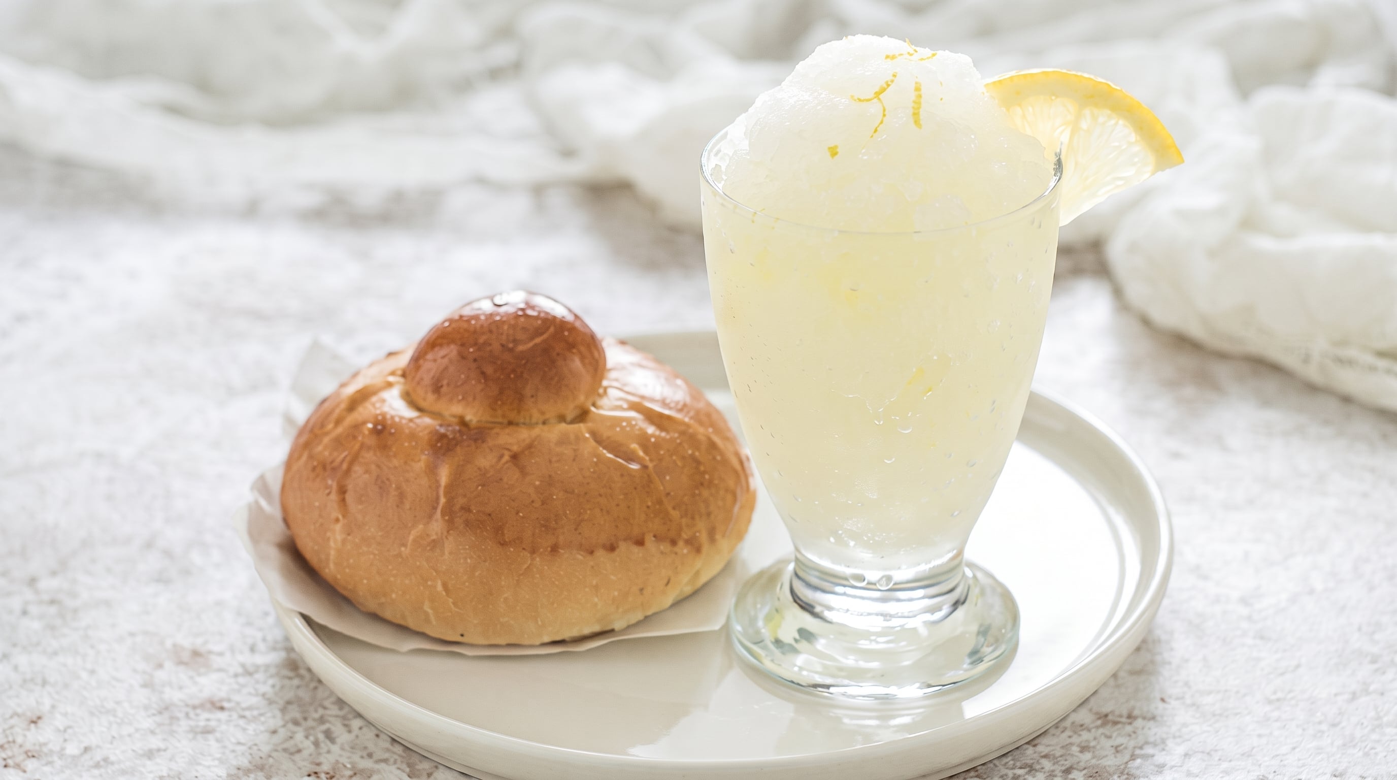 Una copa de granita de limón acompañada por una brioche con tuppo reposa sobre un plato blanco. (Imagen Ilustrativa Infobae)