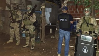 Agentes policiales con uniformes de camuflaje, cascos y chalecos tácticos, algunos armados y con escudo, junto a un oficial de PER, en un entorno oscuro