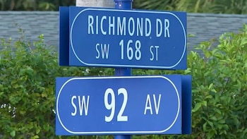 Dos señales de tráfico azules y rectangulares con letras blancas muestran las calles Richmond Dr, SW 168 St y SW 92 Av, montadas en un poste con vegetación