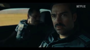 Alfonso Herrera con bigote y camisa oscura mira hacia adelante desde el interior de un automóvil junto a otra persona