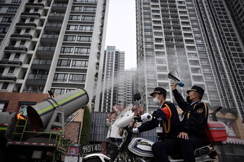 Un hombre que sostiene un altavoz en una motocicleta mientras pasa junto a un vehículo que desinfecta el espacio público cerca de edificios residenciales en el distrito Panyu de Guangzhou (China Daily a través de REUTERS)