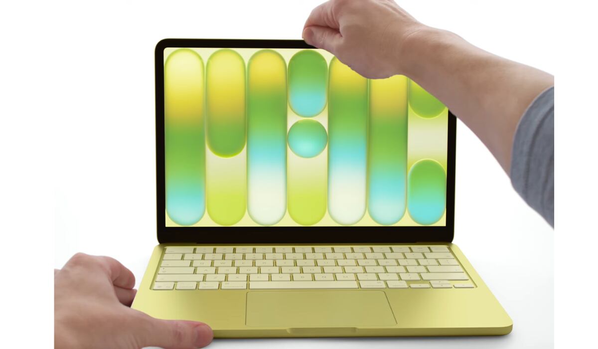Unas manos interactúan con un moderno ordenador portátil amarillo que muestra un fondo de pantalla abstracto. (Apple)