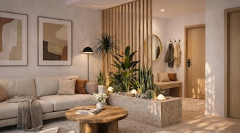 Una sala de estar moderna con sofá beige, mesa de centro de madera, un separador de ambientes con plantas verdes y cactus, un espejo redondo y puertas de madera clara.