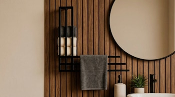 Vista detallada de un baño con pared de listones de madera, un toallero negro vertical y horizontal con toallas, espejo redondo, lavabo blanco y grifo negro.