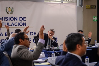 Varios asistentes sentados a una mesa levantan la mano frente a un fondo con la inscripción Comisión de Postulación y el escudo de Guatemala