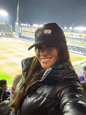 Pampita sonríe a la cámara mientras lleva una gorra negra con el escudo de Boca Juniors y una campera acolchada, con el estadio La Bombonera de fondo