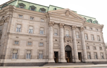 Fachada de un edificio de piedra con columnas, entrada principal, ventanas con persianas y techo verde, con el texto "BANCO DE LA NACION ARGENTINA" en la parte superior