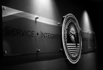 Emblema circular y dos placas en una pared. El emblema indica "FDLE Florida Department of Law Enforcement". Las placas llevan "SERVICE INTEGRITY" y "RESPECT QUALITY"