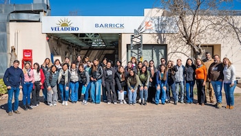 Un grupo numeroso de personas posa de pie frente a un edificio con carteles de Veladero, Barrick y Shandong Gold