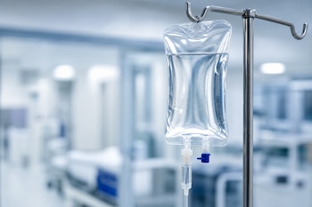 Bolsa transparente con solución salina colgada de un soporte metálico con tubos intravenosos en un hospital.
