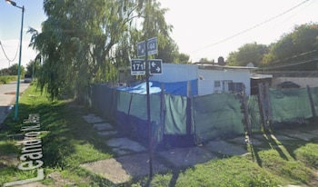 Calle Leandro N. Alem, señalética de calles 44 y 171, vivienda blanca con cerco de malla verde, lona azul, árboles y poste de luz