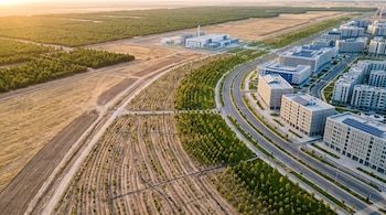 Vista aérea de edificios modernos con paneles solares, avenidas asfaltadas, parcelas aradas con árboles jóvenes y una planta industrial.