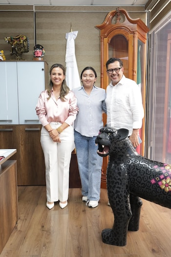 Dos mujeres y un hombre de pie en una oficina con piso de madera junto a una escultura de un jaguar negro