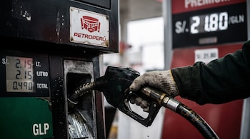 Una mano con guante sostiene una manguera de GLP en un surtidor con el logotipo de Petroperú y pantallas que marcan precios en soles.