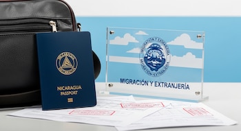 Un pasaporte nicaragüense azul, una bolsa de viaje negra, una placa de Migración y Extranjería de Costa Rica y papeles con sellos rojos sobre una mesa.