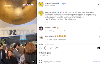 Personas vestidas de luto conversan en una sala funeraria decorada con arreglos de flores blancas y una fotografía enmarcada