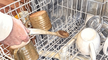 Ilustración en acuarela de una mano que sostiene una cuchara de madera dentro de la bandeja de un lavavajillas con tazas.