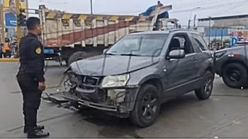 Un agente de policía observa un automóvil gris con el frente destruido en medio de una avenida junto a un camión de carga