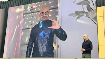 Demis Hassabis en el escenario de Google I/O '26, junto a una pantalla grande que proyecta su reflejo sosteniendo un teléfono con una interfaz luminosa