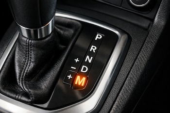 Primer plano de un selector de marchas de carro automático en color negro, con las letras P, R, N, D, M visibles y la letra M iluminada en naranja.
