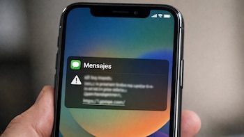 Mano sostiene un teléfono celular con pantalla encendida. La pantalla muestra una notificación de mensaje con un ícono de advertencia y un enlace web borroso.