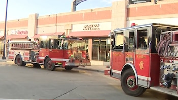 Dos camiones de bomberos rojos con las palabras 'Chicago Fire Dept.' están estacionados en una calle, con edificios comerciales al fondo bajo un cielo claro