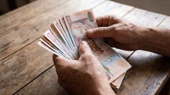 Primer plano de manos de una persona contando una pila de billetes de Quetzal guatemaltecos sobre una superficie de madera rústica.