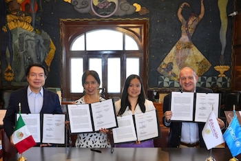 Cuatro personas, dos hombres y dos mujeres, sentadas en sillas de cuero oscuro en una sala con paredes de madera y un mural colorido