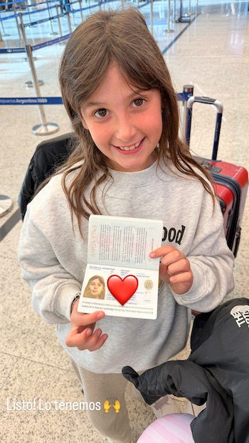 Niña con sudadera gris sostiene un pasaporte argentino abierto. Emoji de corazón rojo sobre la foto. Fondo de aeropuerto con maleta roja y barreras azules