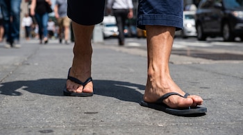 Plano bajo de las piernas y los pies de una persona que camina con sandalias de tira sobre una acera de hormigón.