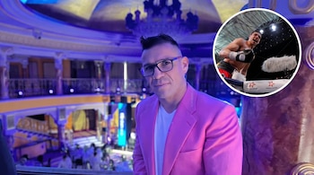 Un hombre con blazer rosa y gafas sonríe en un salón con luces azules y moradas. Un círculo superpuesto muestra un boxeador en un ring.