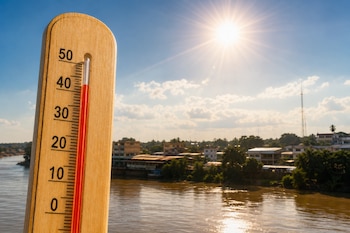 Termómetro de madera con la columna roja en cuarenta grados frente a un río, viviendas y el sol brillante en el cielo.