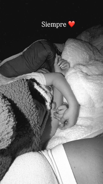 Dos personas cubiertas con mantas, una mano adulta sujeta la de un niño con tatuaje de herradura. Texto "Siempre ❤️". Foto en blanco y negro