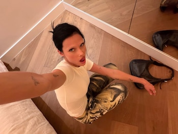 Valentina Zenere, con el pelo recogido y top crema, sentada en un suelo de madera clara, mira a cámara desde arriba; un bolso negro descansa a su lado