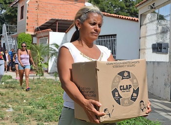 Una mujer sostiene una caja de cartón con el logotipo del programa CLAP y la leyenda Gobierno Bolivariano de Venezuela