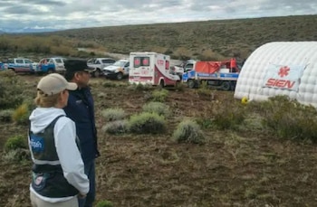 Dos personas observan una carpa médica inflable, una ambulancia y camionetas policiales en un terreno rural