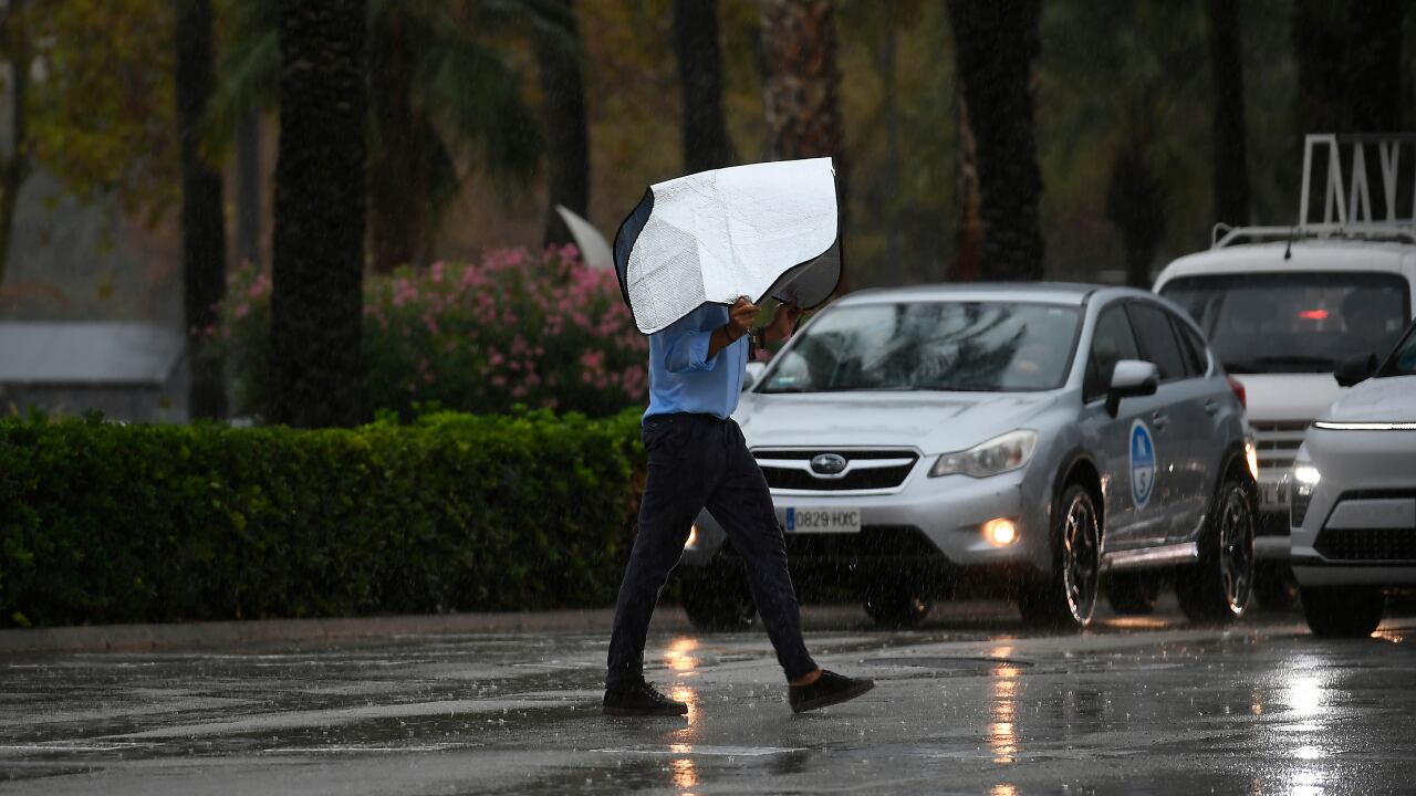 Un hombre se protege de la lluvia con un parasol del coche, en Palma de Mallorca, a 9 de septiembre de 2025 (Miquel A. Borrás/EFE)