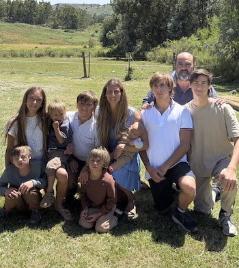 Un grupo familiar compuesto por dos adultos y ocho niños posa sobre el césped en un terreno rural