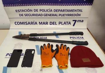 Cizallas, guantes naranjas y negros, un gorro de lana rojo, dos fundas negras de teléfono móvil y un cartel de la Comisaría Mar del Plata 7ma