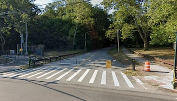Un cruce de camino con un paso de cebra pintado en blanco, bloqueado por dos barreras con bandas rojas y blancas, y un letrero amarillo de "ROAD CLOSED"