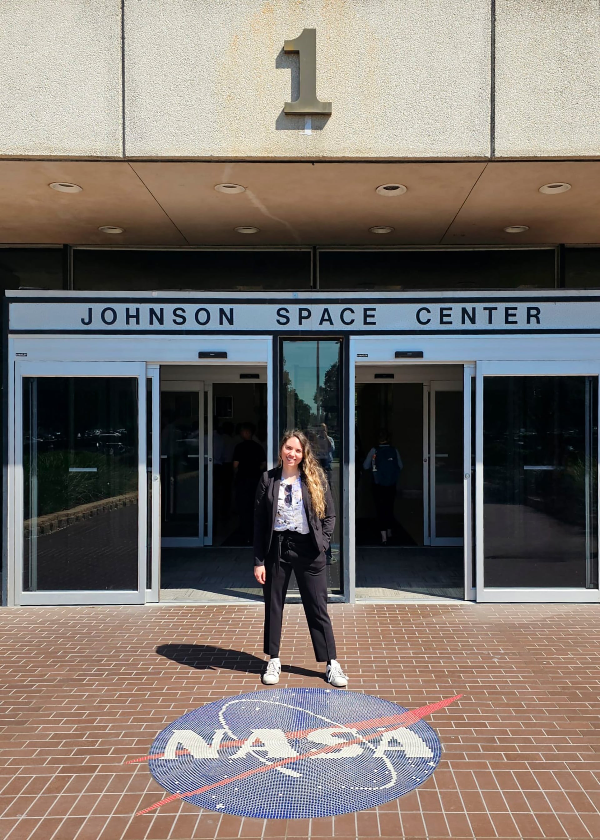 Lorna posa sonriente frente a la entrada principal del Centro Espacial Johnson de la NASA, con el icónico logotipo en el suelo