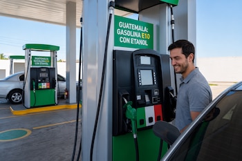 Un hombre sostiene la manguera de un dispensador de combustible con un letrero que indica gasolina E10 con etanol junto a un automóvil.