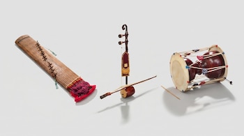 Vista aérea de un gayageum de madera, un haegeum marrón con su arco y un janggu de tambor con una baqueta, sobre un fondo blanco.