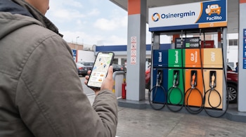 Una persona sostiene un teléfono con un mapa frente a surtidores de combustible identificados con los letreros de Osinergmin y Facilito.