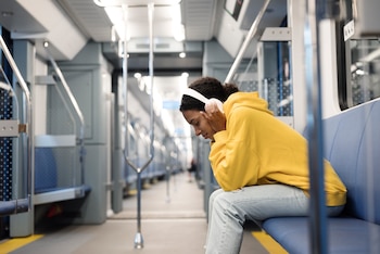 Una mujer en un vagón del metro con unos cascos escuchando música.