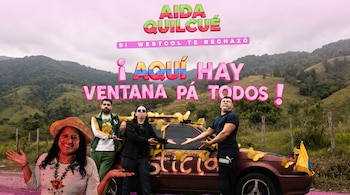 Aída Quilcué, con sombrero y camisa bordada, sonríe junto a tres hombres de pie frente a un coche rojo decorado con mariposas y banderas de Colombia, con montañas.