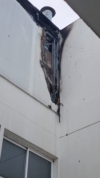 Humo gris que sale de la terraza de un edificio y toma cercana de una pared exterior carbonizada con hollín y estructuras dañadas