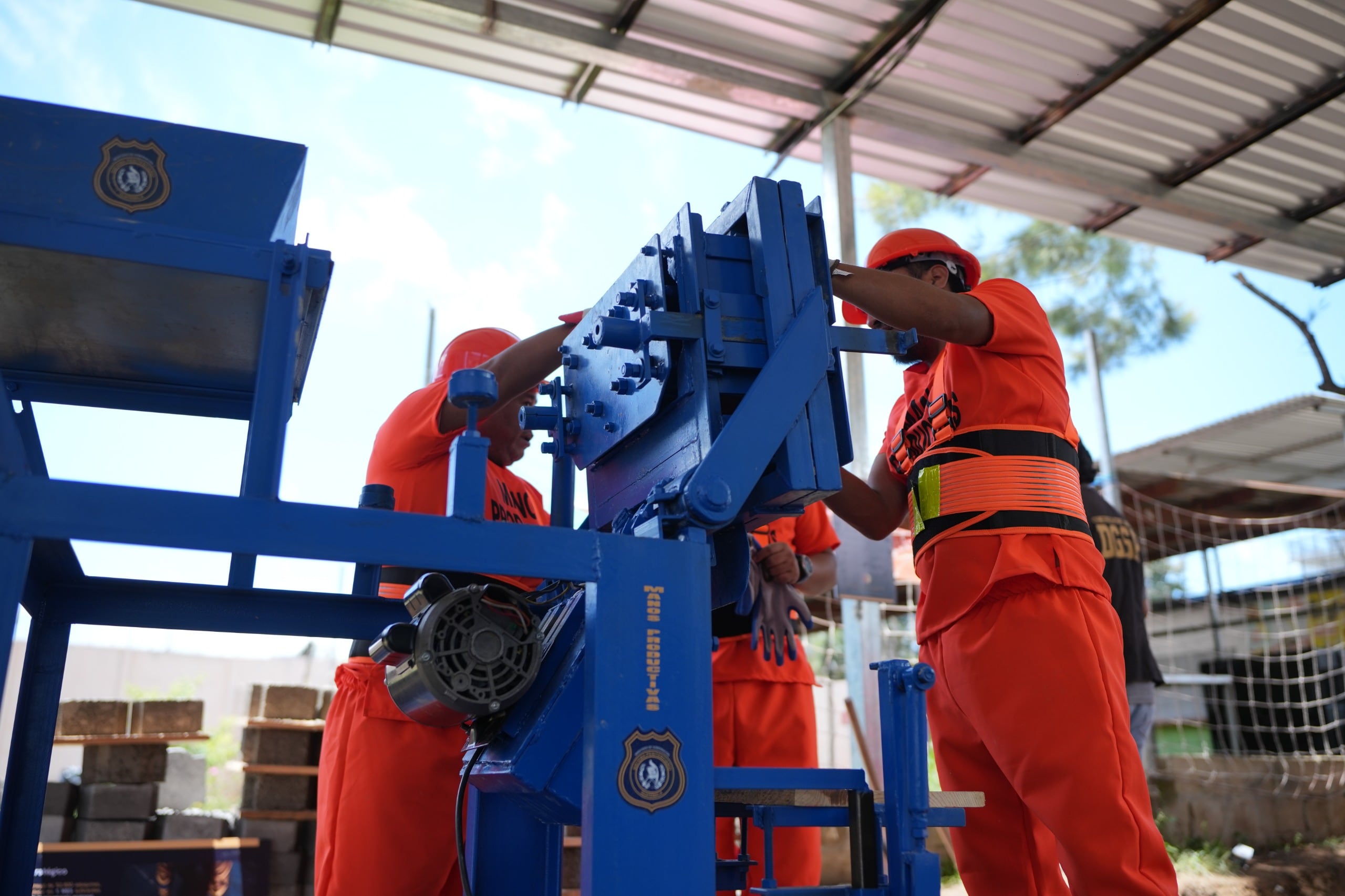 Personal del programa Manos Productivas, de la Dirección General de Centros Penales de El Salvador, opera una máquina industrial para la fabricación de productos, con bloques apilados al fondo. (Ministerio de Gobernación )