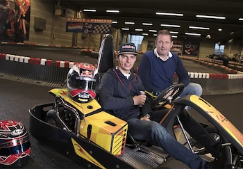 Max Verstappen y Jos Verstappen posan junto a un kart amarillo y dos cascos en una pista de carreras bajo techo